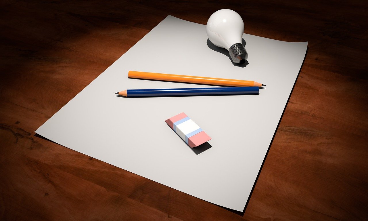 Papel de folha branco sobre uma mesa com dois lápis, uma lâmpada e borracha em cima